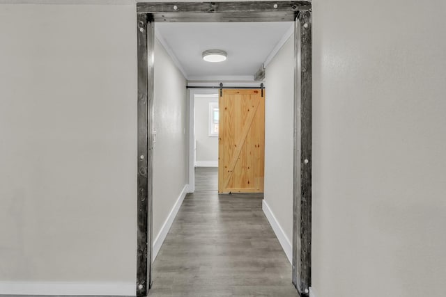 hall with a barn door, crown molding, baseboards, and wood finished floors