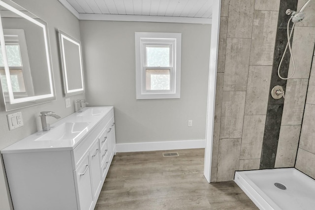 full bathroom with visible vents, a sink, a tile shower, wood finished floors, and baseboards