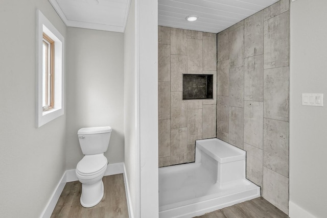 bathroom with a tile shower, wood finished floors, toilet, and baseboards