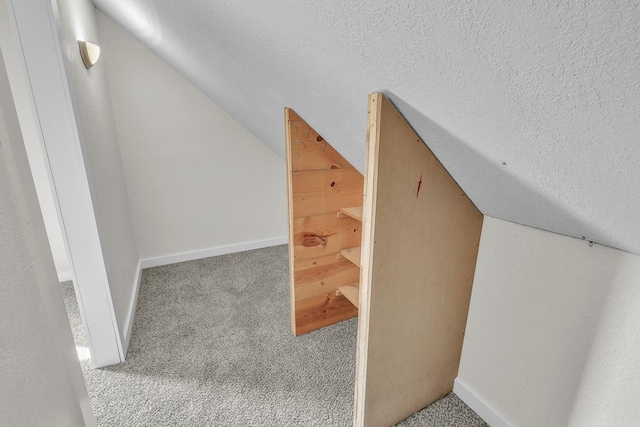 interior space with a textured ceiling, vaulted ceiling, carpet flooring, and baseboards