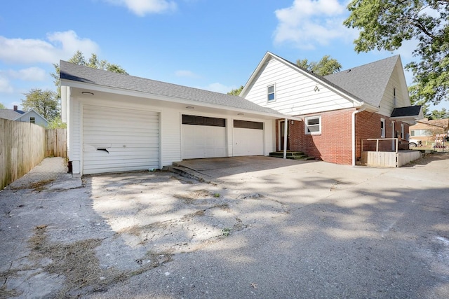 exterior space featuring a garage, driveway, a shingled roof, fence, and brick siding