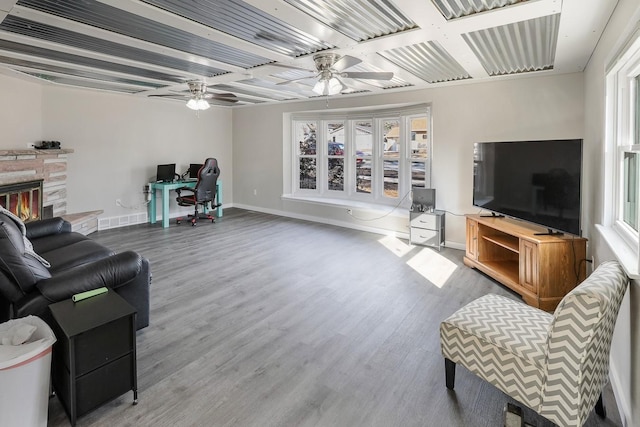 living room featuring a ceiling fan, a stone fireplace, baseboards, and wood finished floors