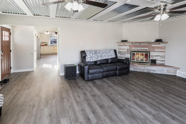 living room featuring ceiling fan, a fireplace, baseboards, and wood finished floors