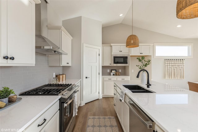 kitchen with wall chimney exhaust hood, sink, decorative light fixtures, vaulted ceiling, and appliances with stainless steel finishes