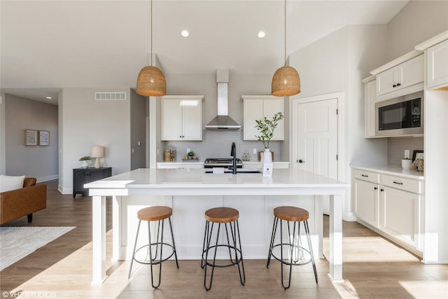 kitchen featuring pendant lighting, backsplash, black microwave, a center island with sink, and wall chimney exhaust hood