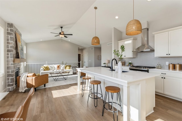 kitchen with wall chimney exhaust hood, sink, decorative light fixtures, stainless steel range with gas stovetop, and an island with sink