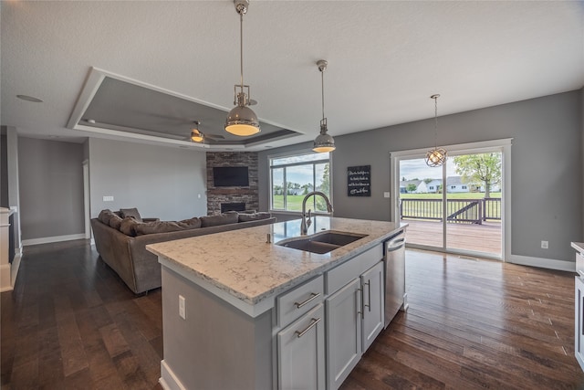 kitchen with stainless steel dishwasher, decorative light fixtures, an island with sink, a raised ceiling, and sink