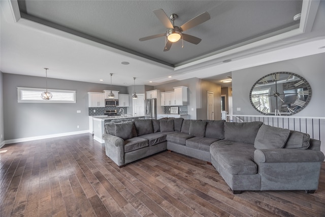 living room with dark hardwood / wood-style flooring, a raised ceiling, and ceiling fan