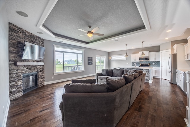 living room with a tray ceiling, ceiling fan, dark hardwood / wood-style floors, a fireplace, and a textured ceiling