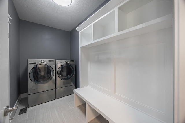 clothes washing area with washing machine and dryer, baseboards, a textured ceiling, and laundry area