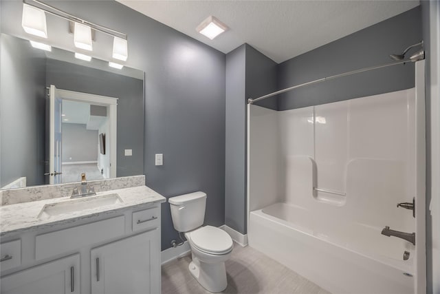 bathroom with a textured ceiling, vanity,  shower combination, baseboards, and toilet