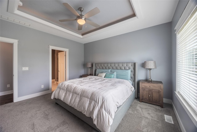 carpeted bedroom with visible vents, baseboards, a ceiling fan, and a tray ceiling