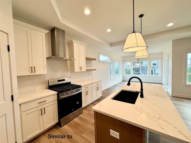 kitchen featuring pendant lighting, wall chimney range hood, white cabinetry, sink, and stainless steel range with gas stovetop