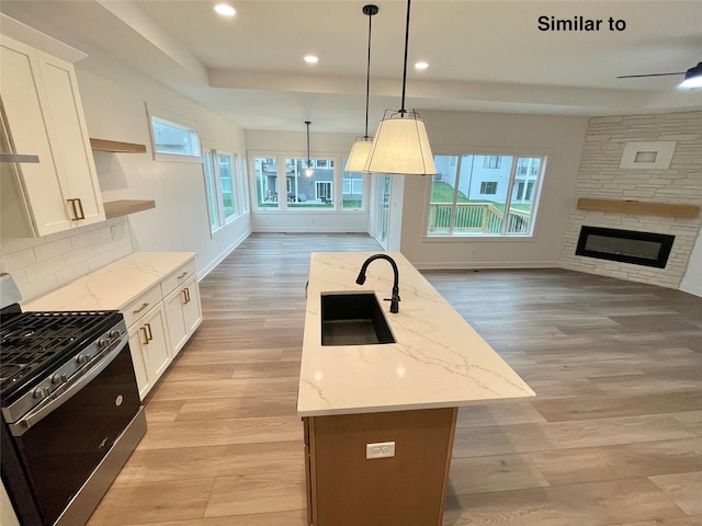 kitchen with decorative light fixtures, sink, white cabinets, and stainless steel gas range oven