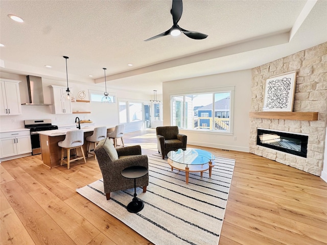 living area featuring recessed lighting, a fireplace, light wood-style floors, a textured ceiling, and a ceiling fan