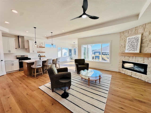 living room with light wood-type flooring, a textured ceiling, a stone fireplace, and a ceiling fan