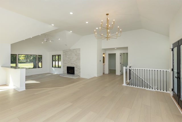 unfurnished living room featuring ceiling fan with notable chandelier, light hardwood / wood-style flooring, a stone fireplace, and high vaulted ceiling