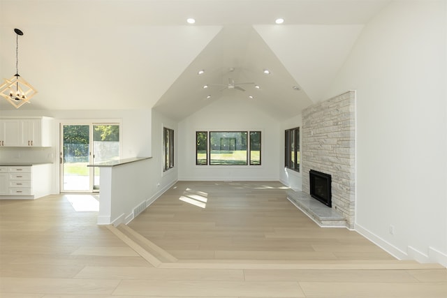 unfurnished living room featuring a fireplace, high vaulted ceiling, light hardwood / wood-style floors, and ceiling fan with notable chandelier