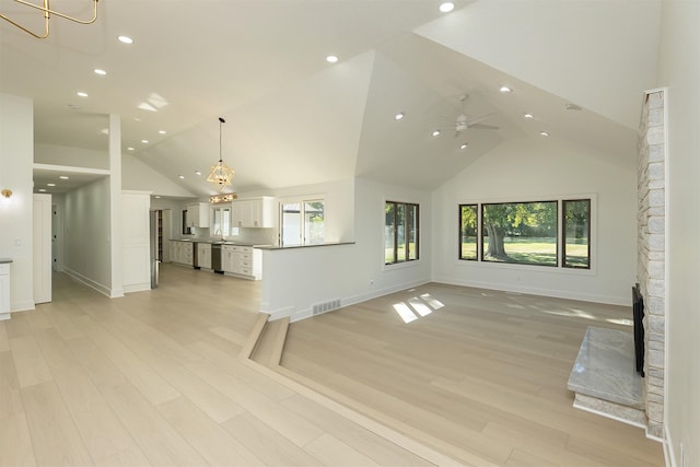 unfurnished living room featuring ceiling fan with notable chandelier, light hardwood / wood-style floors, and high vaulted ceiling