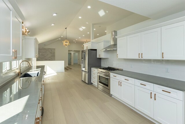 kitchen featuring hanging light fixtures, wall chimney exhaust hood, decorative backsplash, appliances with stainless steel finishes, and white cabinetry