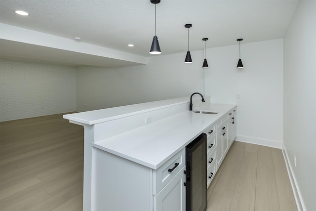 kitchen with brick wall, beverage cooler, sink, pendant lighting, and white cabinets