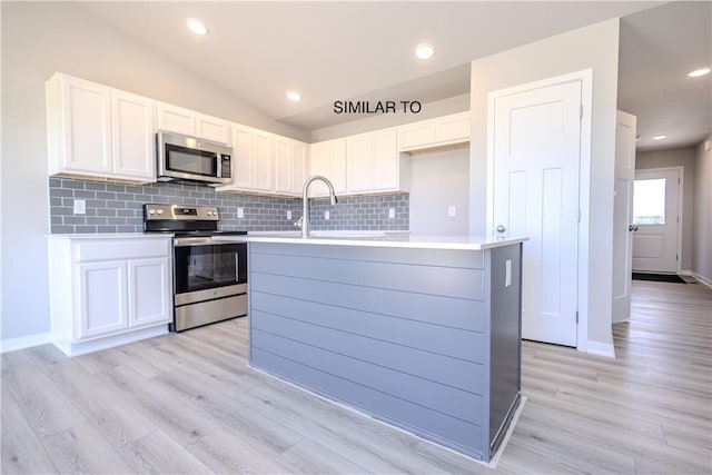 kitchen featuring white cabinetry, a center island with sink, stainless steel appliances, and light wood-type flooring