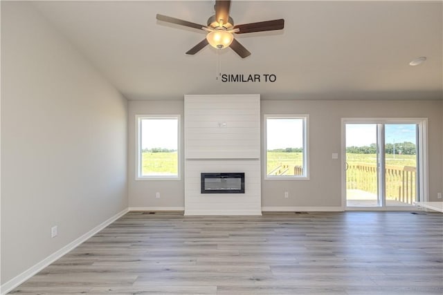 unfurnished living room featuring ceiling fan, a large fireplace, a healthy amount of sunlight, and light hardwood / wood-style floors