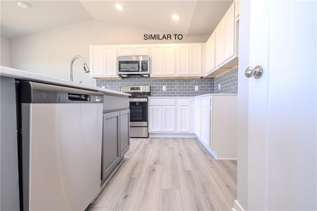 kitchen featuring lofted ceiling, white cabinets, tasteful backsplash, light hardwood / wood-style floors, and stainless steel appliances