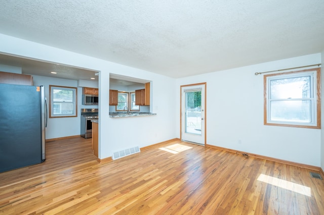 unfurnished living room featuring light wood-type flooring, a textured ceiling, and sink