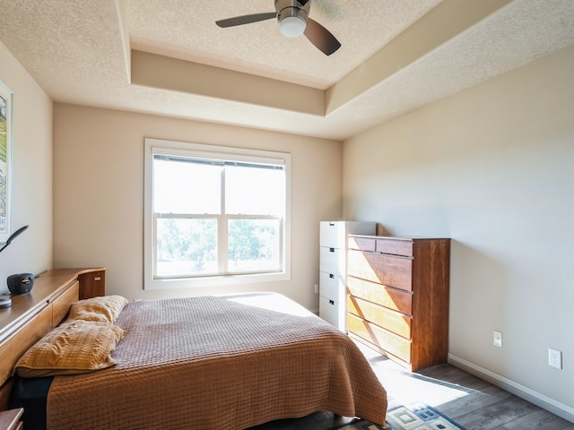 bedroom with ceiling fan, a textured ceiling, a tray ceiling, and hardwood / wood-style floors