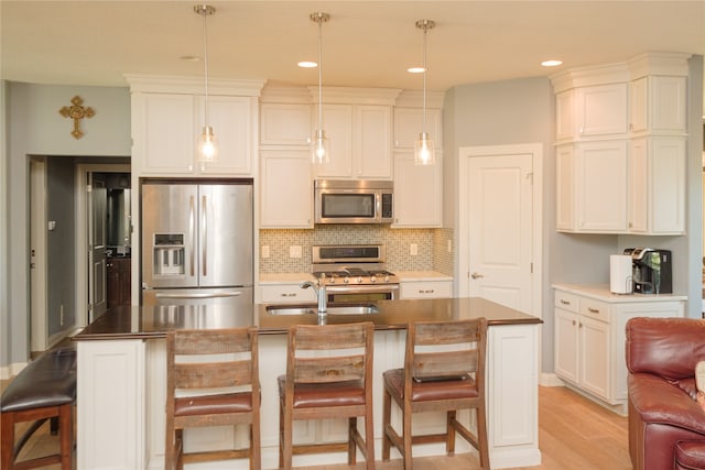 kitchen featuring an island with sink, hanging light fixtures, stainless steel appliances, a breakfast bar, and light hardwood / wood-style floors