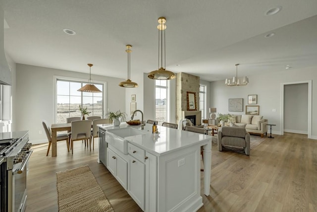 kitchen featuring white cabinetry, stainless steel appliances, a kitchen island with sink, a large fireplace, and hanging light fixtures