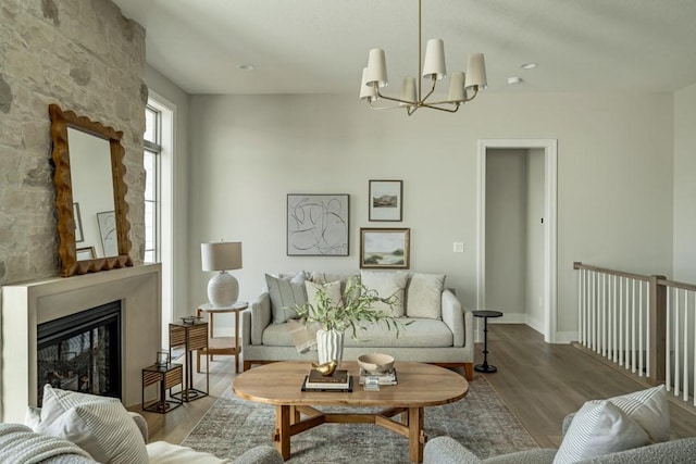 living room with hardwood / wood-style flooring, a stone fireplace, and a notable chandelier