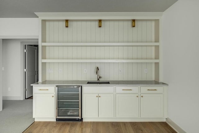 bar with sink, white cabinetry, beverage cooler, and light carpet