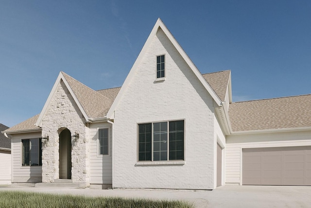 view of front of home with brick siding, driveway, an attached garage, and roof with shingles