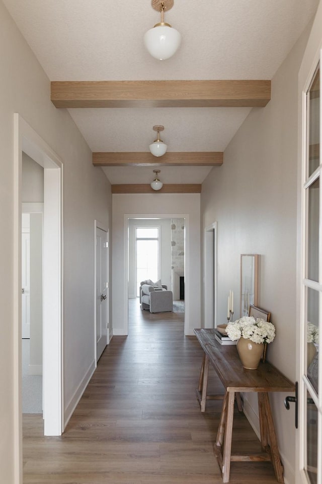 corridor featuring light wood-type flooring, beam ceiling, and baseboards