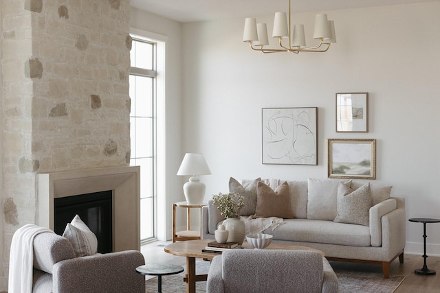 living area with a glass covered fireplace, a notable chandelier, baseboards, and wood finished floors