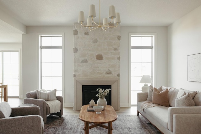 living area with a notable chandelier, a fireplace, wood finished floors, and a healthy amount of sunlight