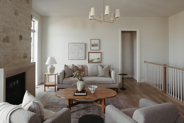 living room featuring baseboards, wood finished floors, a glass covered fireplace, and an inviting chandelier