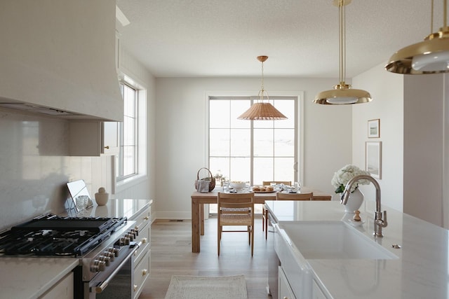 kitchen featuring a textured ceiling, a sink, light wood-style floors, hanging light fixtures, and stainless steel range