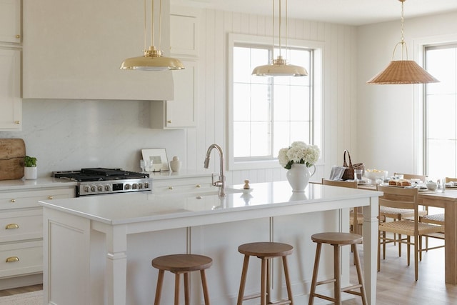 kitchen featuring stove, a kitchen breakfast bar, a kitchen island with sink, light countertops, and a sink