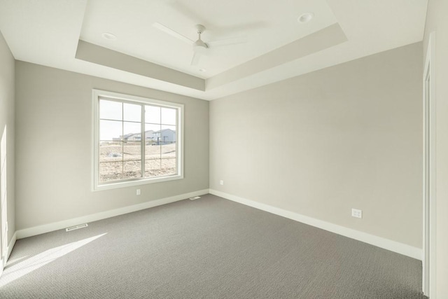 carpeted spare room featuring ceiling fan, a raised ceiling, and baseboards