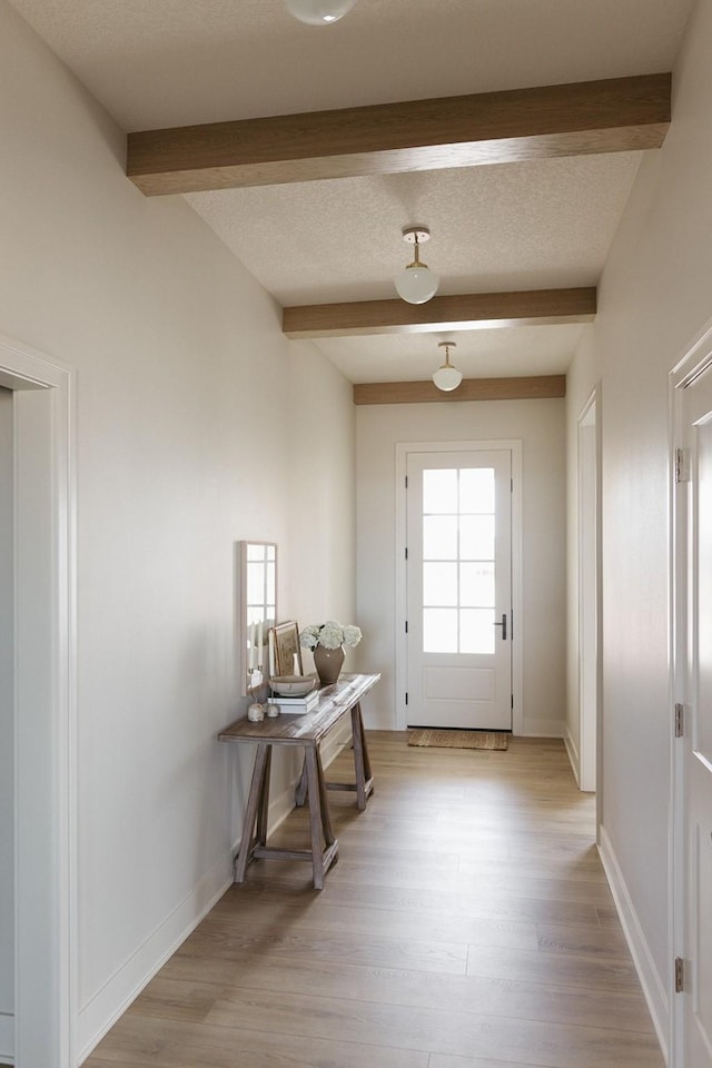 entryway featuring light wood-type flooring, beam ceiling, a textured ceiling, and baseboards