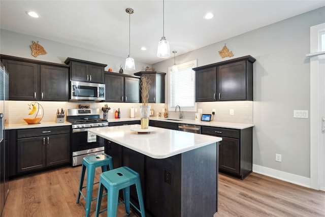 kitchen with light wood-type flooring, a center island, sink, appliances with stainless steel finishes, and decorative light fixtures