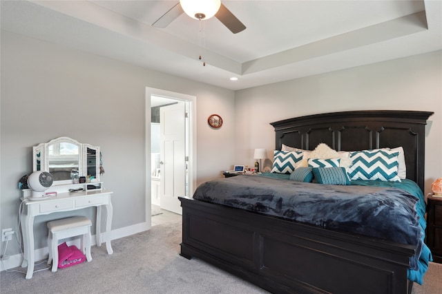 carpeted bedroom featuring a raised ceiling, ensuite bath, and ceiling fan