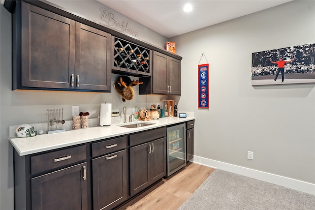 bar with light wood-type flooring, dark brown cabinetry, sink, and wine cooler