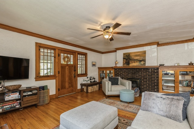 living room with a brick fireplace, a textured ceiling, ceiling fan, ornamental molding, and hardwood / wood-style floors