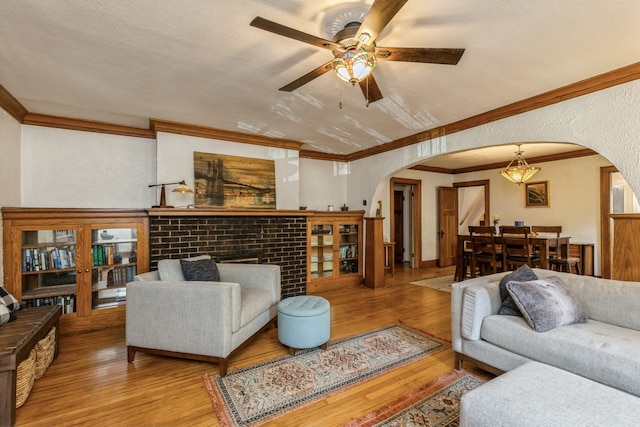 living room featuring a textured ceiling, a fireplace, light hardwood / wood-style flooring, crown molding, and ceiling fan