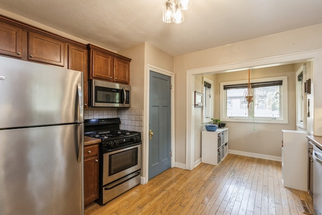 kitchen featuring pendant lighting, a textured ceiling, backsplash, stainless steel appliances, and light wood-type flooring