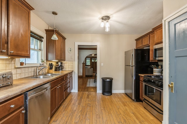 kitchen with tasteful backsplash, stainless steel appliances, light hardwood / wood-style flooring, decorative light fixtures, and sink